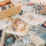 Creative setup of watercolor art supplies with paintings on a glass table.