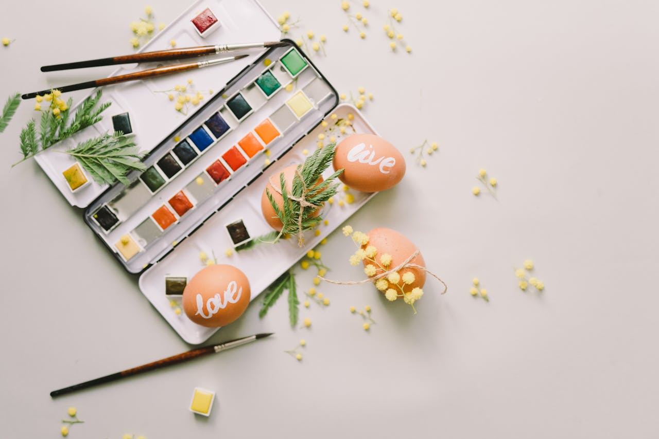 Easter eggs with 'love' text and paint palette in a spring-themed creative flat lay scene.